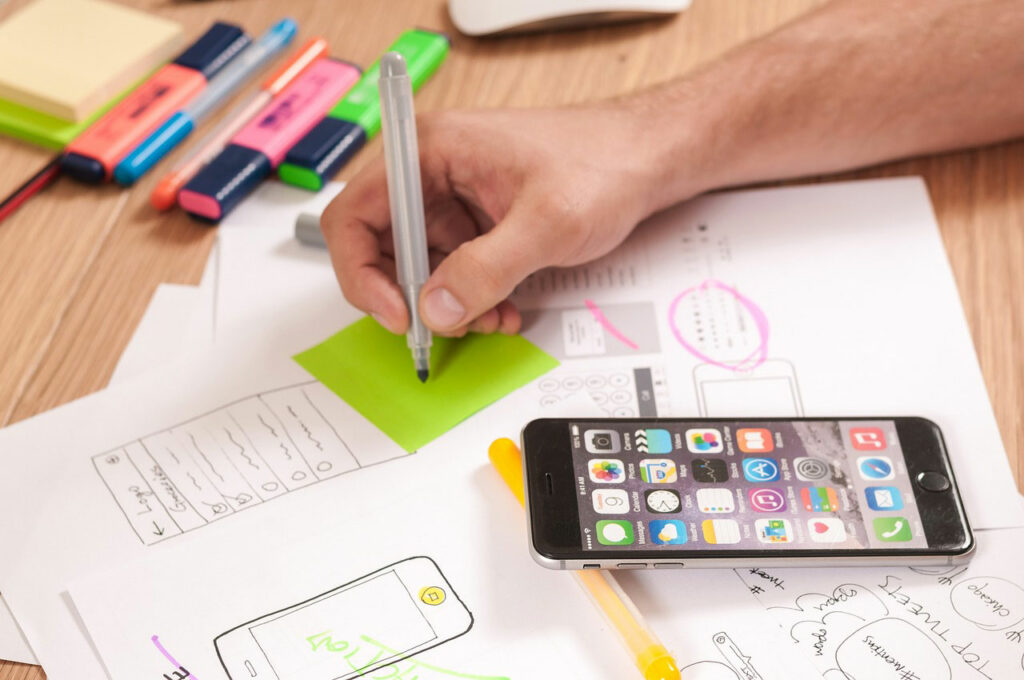 Schreibtisch mit Sketch-Entwürfen für Webdesign auf Mobilgeräten & Stiften, um das Website Branding auszuarbeiten